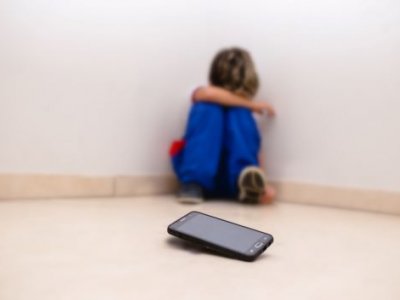 Upset child sits away from cell phone device 